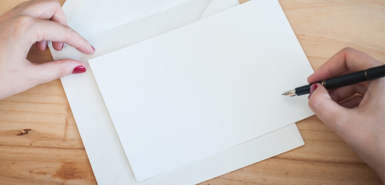 Person with pencil writing on blank envelope. What to Write in a Condolence or Sympathy Card.